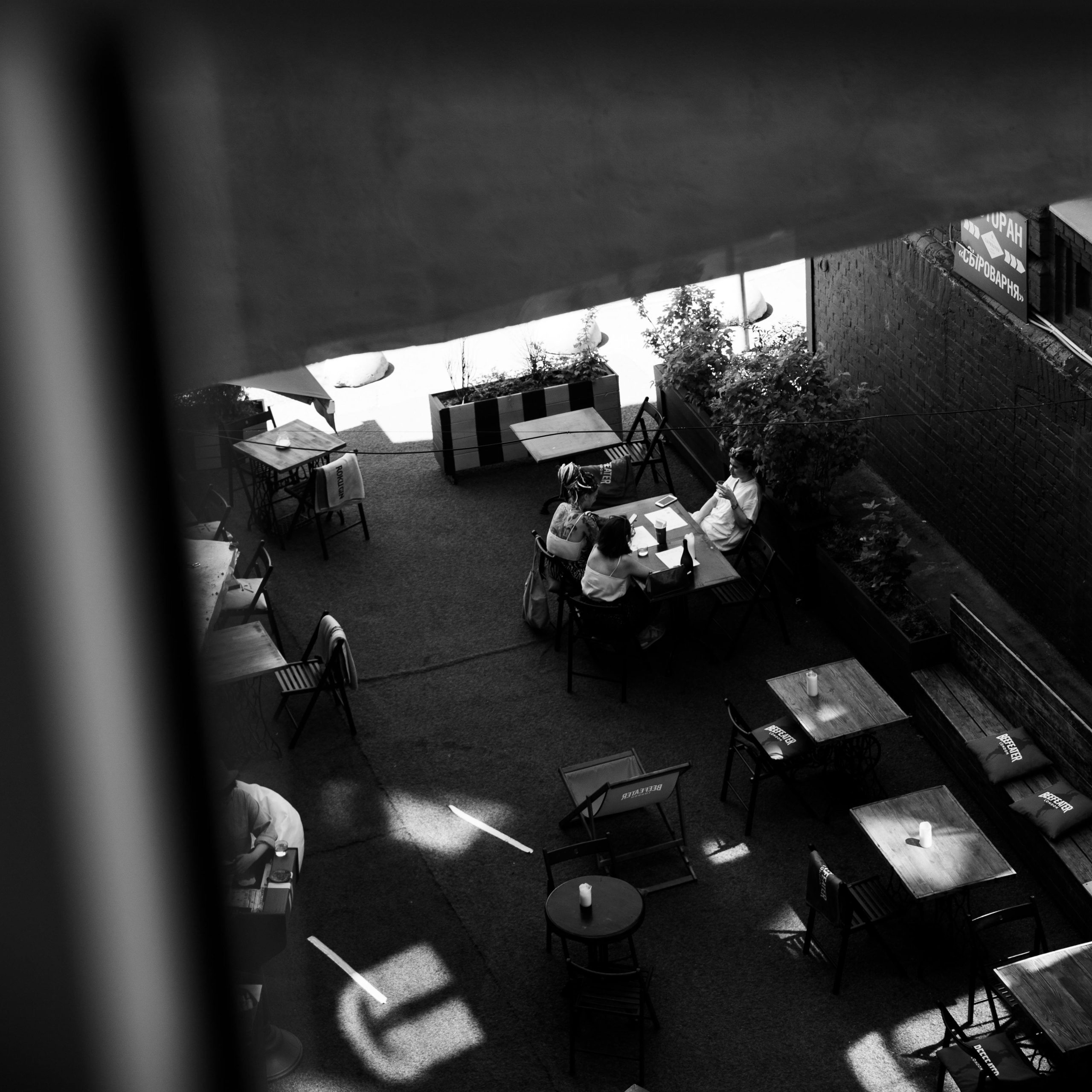 Black and white aerial shot of people dining at an outdoor cafe with tables and chairs.